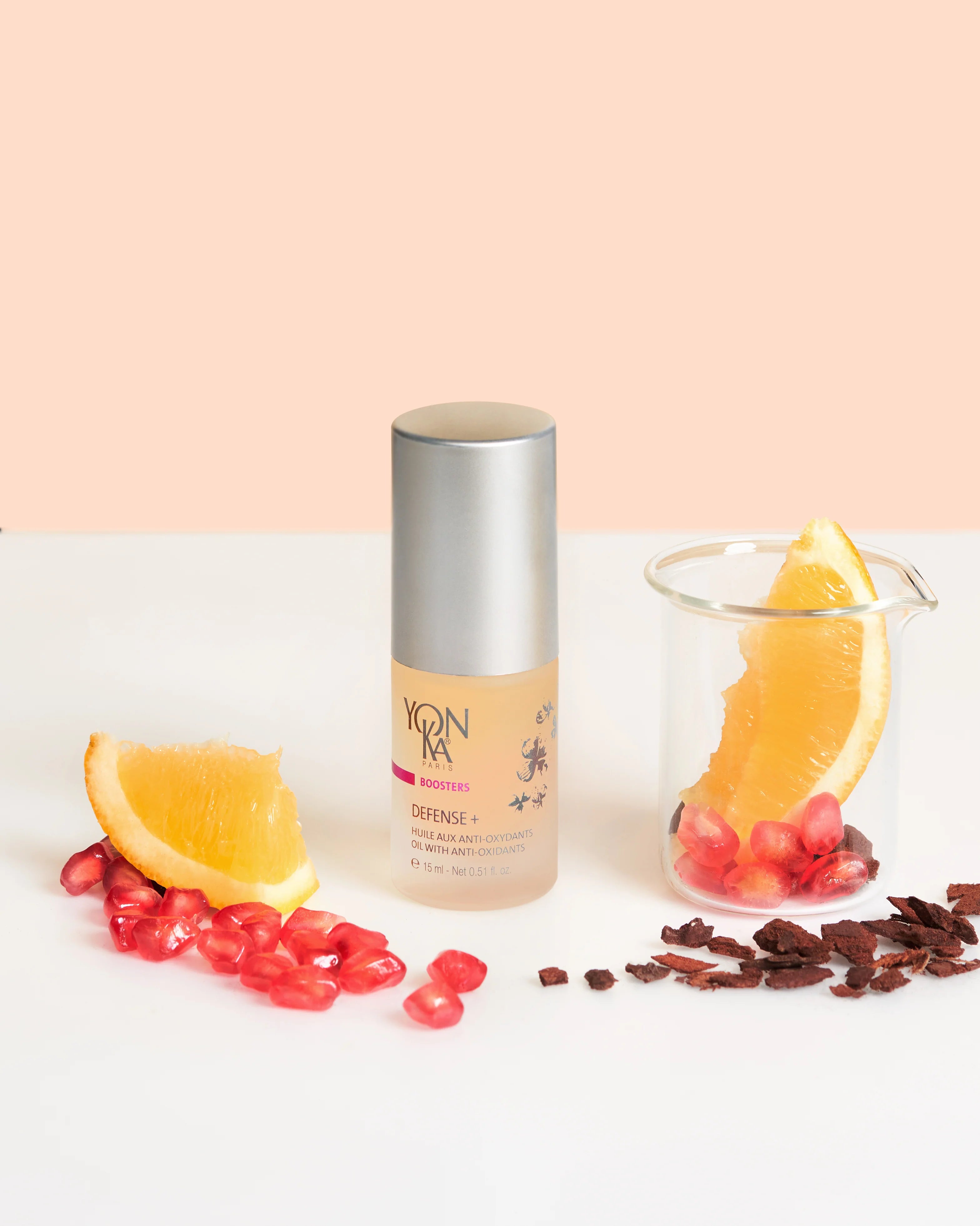 Skincare bottle with oranges and pomegranate seeds on a white surface