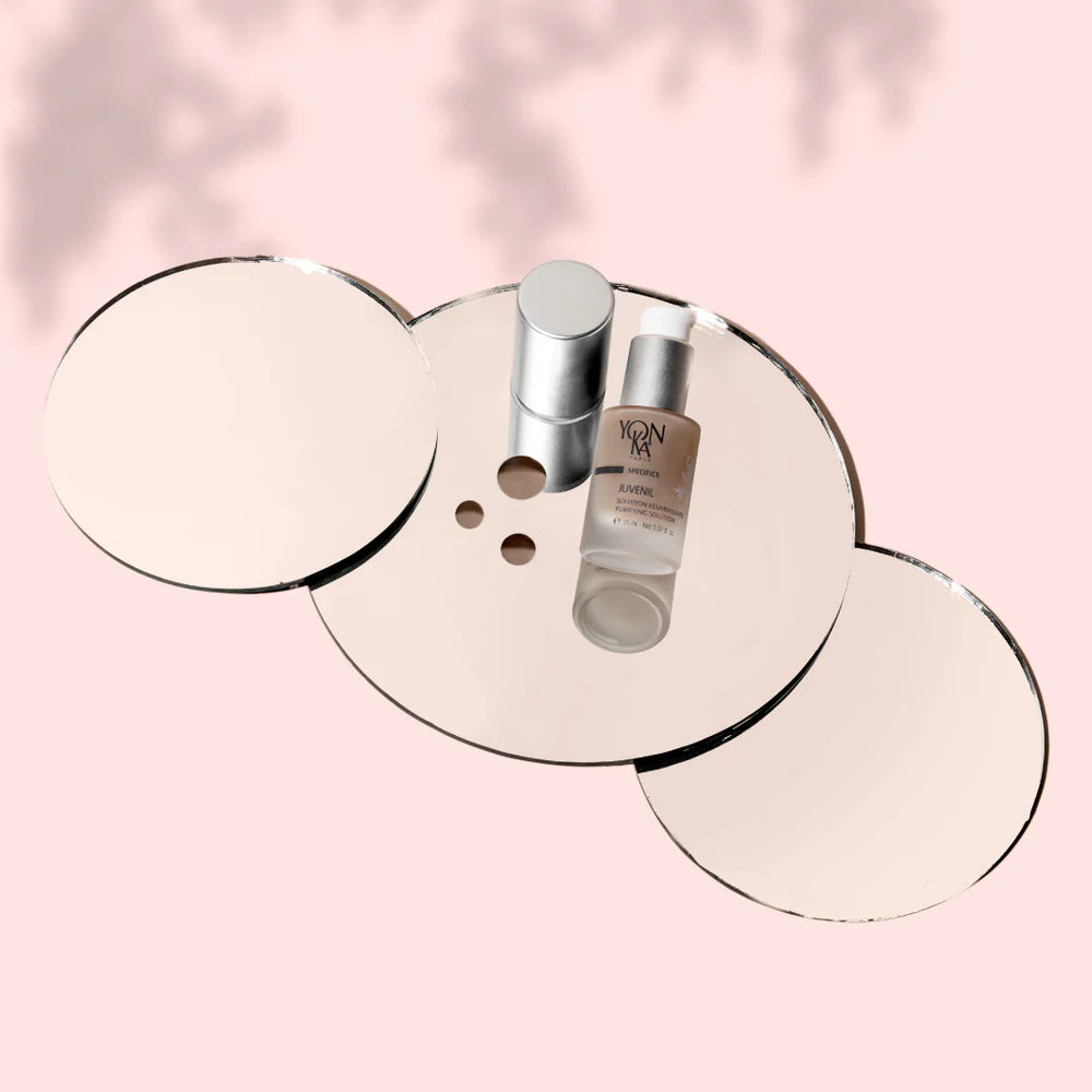 Skincare products on a round mirror with a pink background