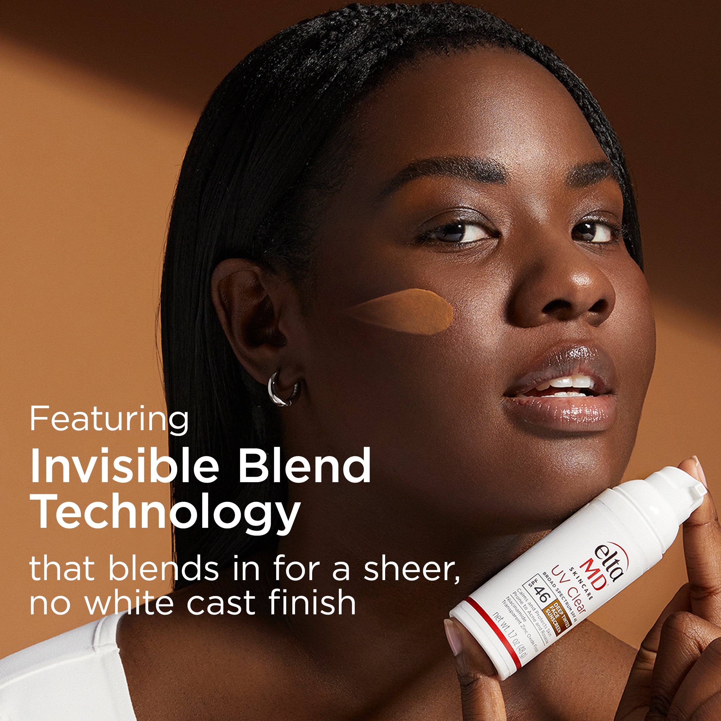 Woman applying makeup with a tube labeled 'Invisible Blend Technology' on a brown background