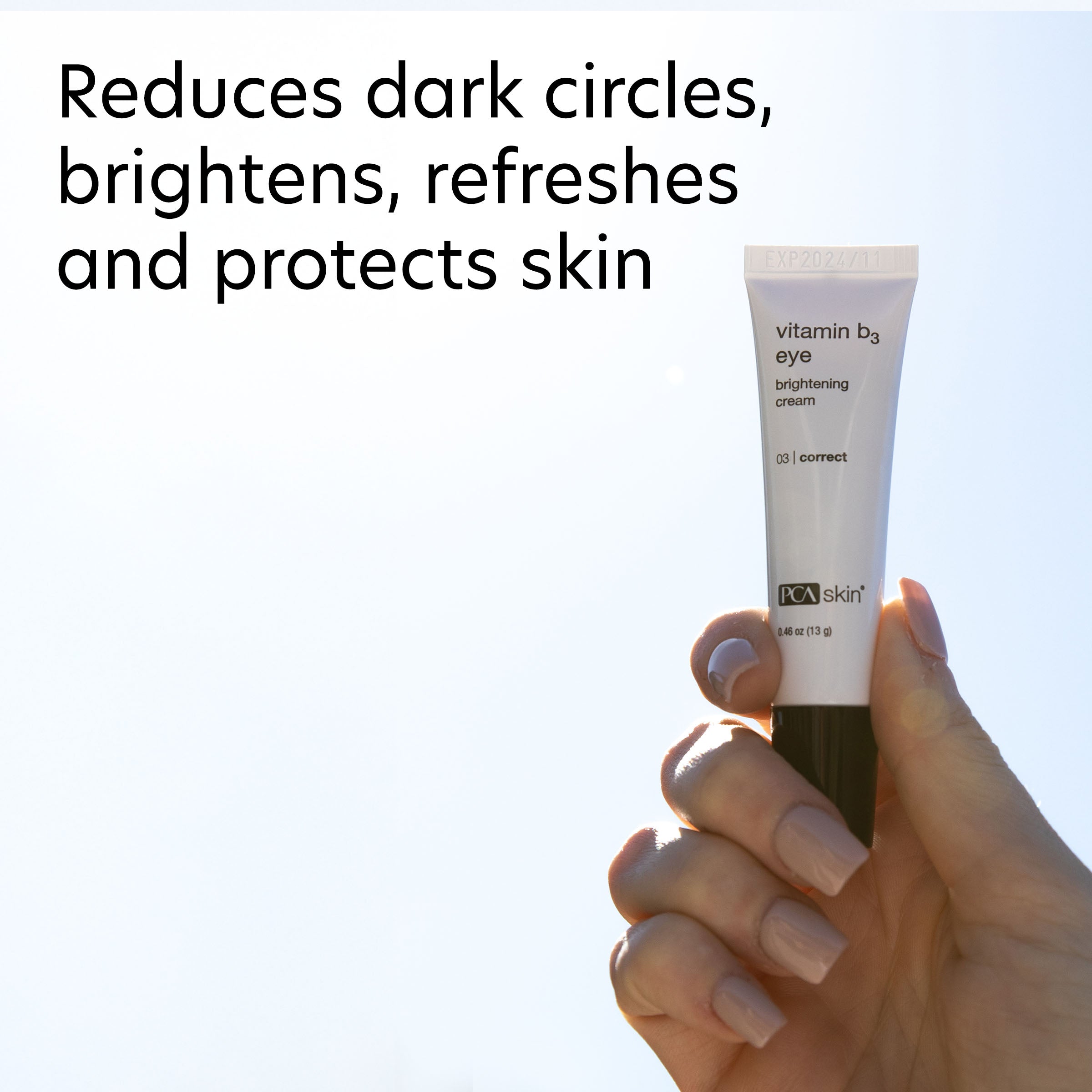 Hand holding a tube of PCA Skin vitamin B3 eye brightening cream against a light blue background.